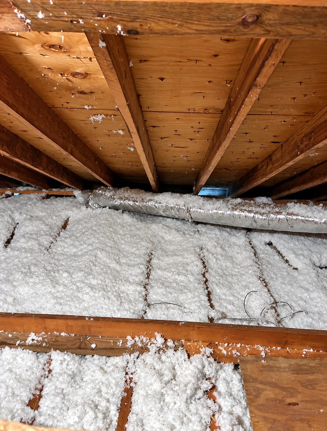 Blown-in insulation between ceiling joists with insulated duct running across
